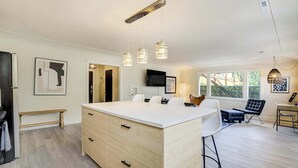A modern kitchen with a central island, pendant lighting, and a dining area with chairs and a table.