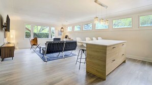 A modern kitchen with a central island, a dining area with chairs, a black chair, and a desk with a lamp.