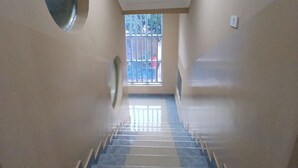 Un passadís amb una finestra circular, una porta i una escala que condueix a un balcó.