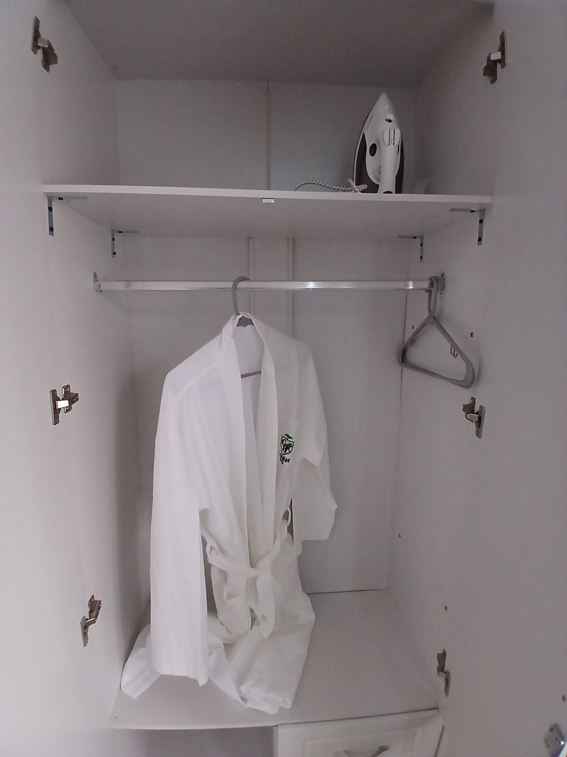 A white robe hanging on a hook, a white shelf with a white object, and a white wall with a hook.