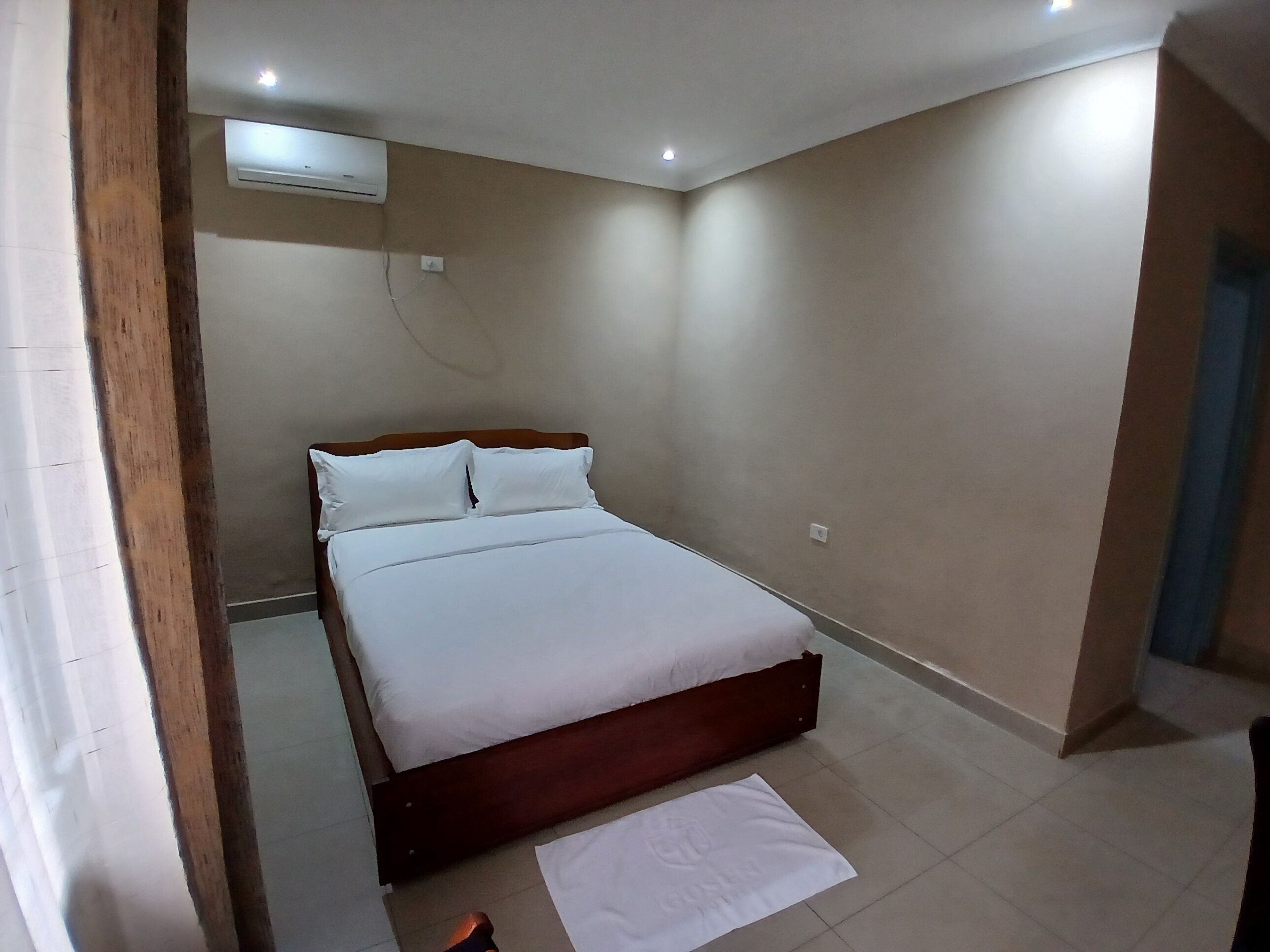 A bedroom with a bed, a wooden headboard, a white mattress, and a white blanket.
