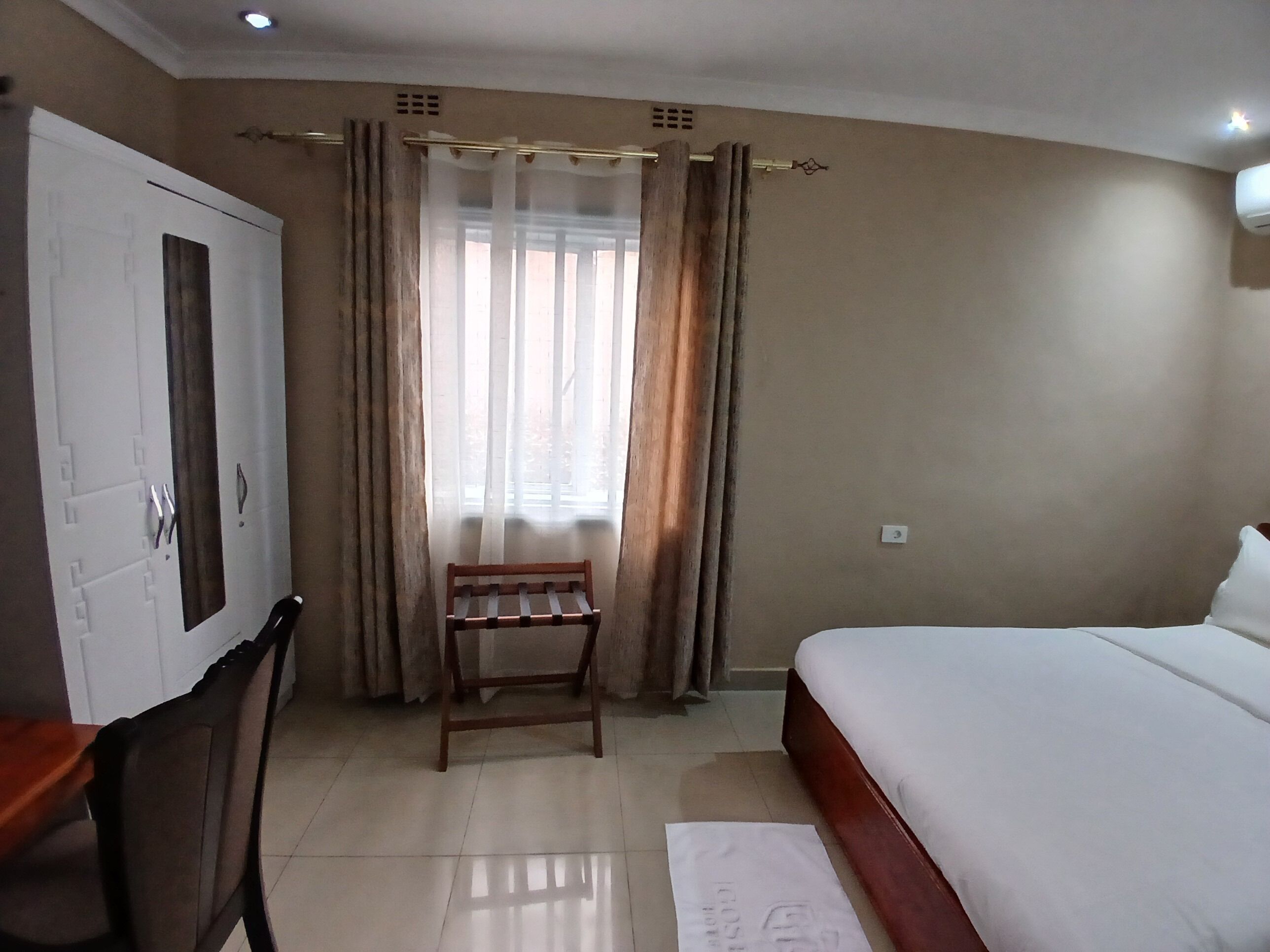 Un dormitorio con una cama, una silla de madera, un armario y una ventana con cortinas.