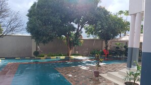 Una piscina amb una terrassa enrajolada, envoltada de plantes en testos i un arbre.