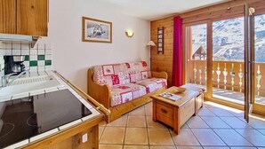 Una stanza accogliente con angolo cottura, divano, un tavolino e un balcone con vista sulle montagne.