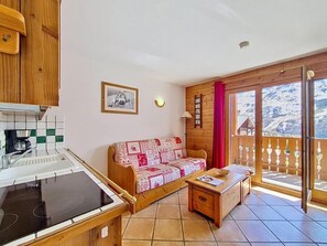 Ein gemütliches Zimmer mit einer Küchenzeile, einem Sofa, einem kleinen Tisch und einem Balkon mit Bergblick.