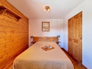 Ein Schlafzimmer mit einem hölzernen Kopfstück, einem gerahmten Bild an der Wand und einem Tablett mit Tasse und Glas auf dem Bett.