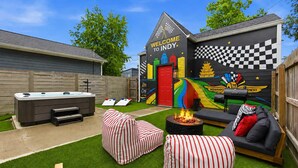 Ein Garten mit Whirlpool, gestreiften Kissen, einer Feuerstelle und einem Wandbild mit der Aufschrift 'Welcome to Indy'.