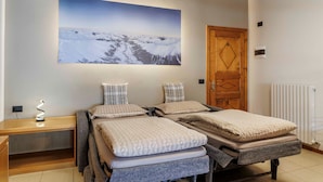 Ein Zimmer mit zwei Betten, einem Holztisch, einem großen Landschaftsbild, einer Holztür und einer Heizung.