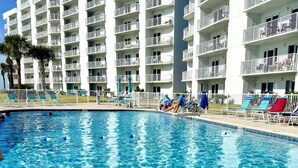 Une piscine à l’eau d’un bleu cristallin, entourée d’un bâtiment blanc doté de balcons et d’un espace clos aménagé avec des chaises longues.