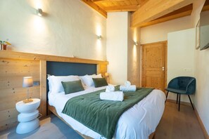 Ein Schlafzimmer mit Bett, Nachttischlampen, einem Sessel und einer Holztür.
