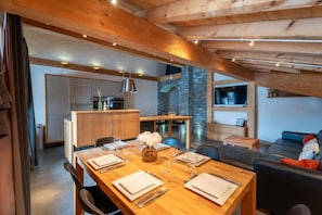 A modern kitchen with wooden cabinets, a stone accent wall, and a dining area with a wooden table set for four. - 2nd floor, hammam, balcony, parking, 95m², Les Gets (Les Gets)