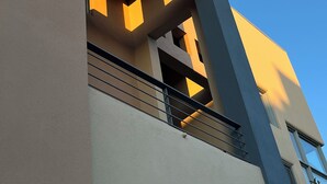 A modern building with a flat facade, large windows, and a balcony with a railing.