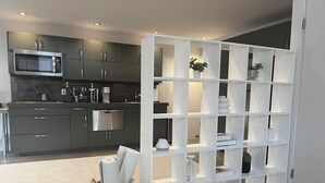 A modern kitchen with grey cabinets, a microwave, and a white shelving unit with decorative items.