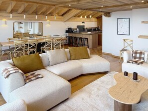 Ein modernes Wohnzimmer mit einem Ecksofa, einem Essbereich mit Holztisch und einer Küche im Hintergrund.