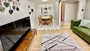 A living room with a TV, wooden dining table, chairs, a green sofa, and a patterned rug. - Cozy Spacious Quiant 2-bed 2-bath apartment. (Wilmington)