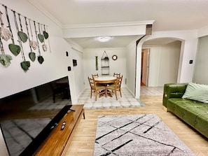A living room with a TV, wooden dining table, chairs, a green sofa, and a patterned rug.