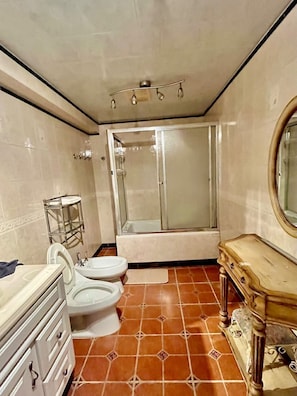 A bathroom with a toilet, bidet, vanity, and a shower with a glass door.