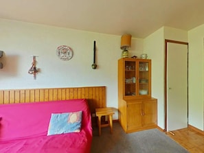 Ein Schlafzimmer mit Holzkopfende, einem Bett mit rosa Bettwäsche, einem kleinen Holztisch, einem Schrank mit Gläsern und einer Tür.