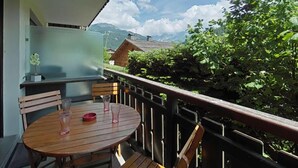 Um deck de madeira com mesa e cadeiras, com vista para uma paisagem montanhosa.