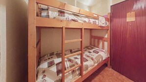 Uma cama beliche com um edredom estampado, uma escada de madeira e uma porta vermelha em um quarto com piso de madeira.