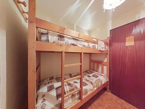 Ein Stockbett mit einem gemusterten Quilz, einer Holzleiter und einer roten Tür in einem Zimmer mit Holzboden.