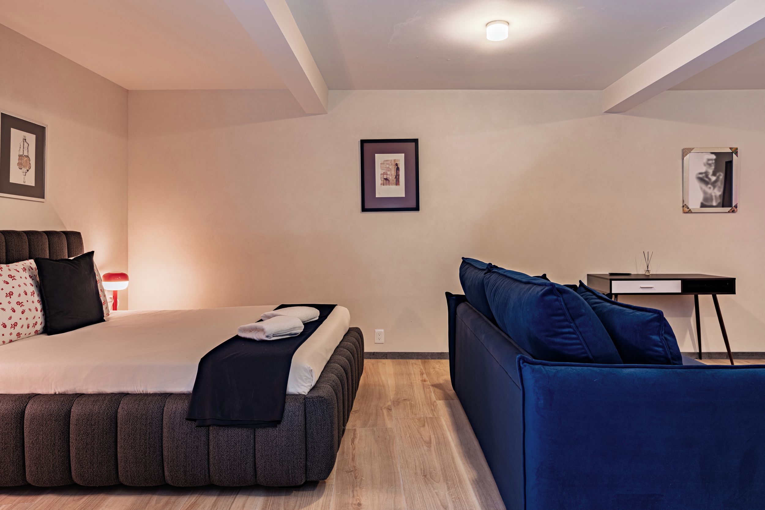 A modern bedroom with a bed, a blue sofa, a desk, and framed artwork on the walls.