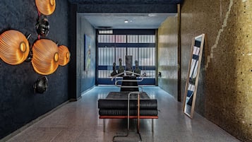 Un hall d’entrée moderne avec un canapé en cuir noir, un grand miroir et des appliques murales décoratives.