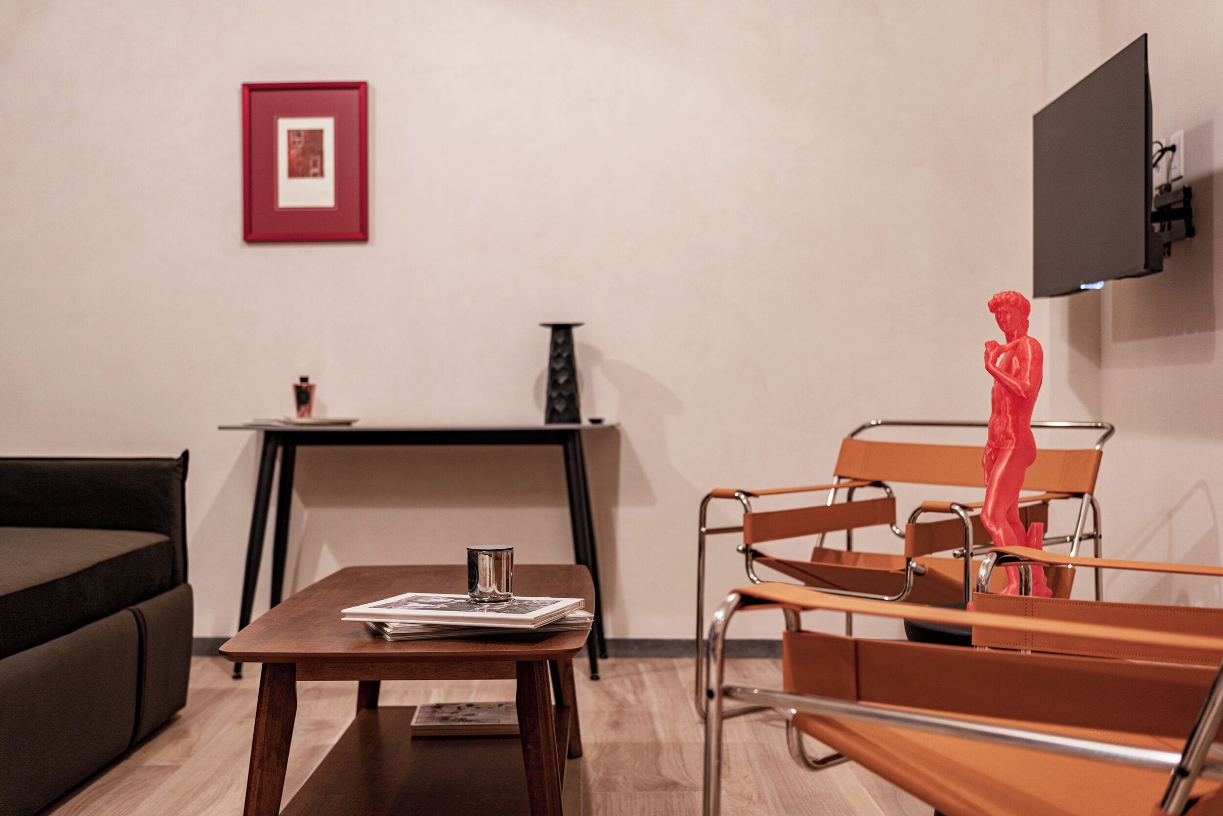 Une pièce moderne avec un canapé marron, une table en bois sur laquelle sont posés des magazines, une sculpture rouge, un téléviseur noir et un tableau encadré accroché au mur.