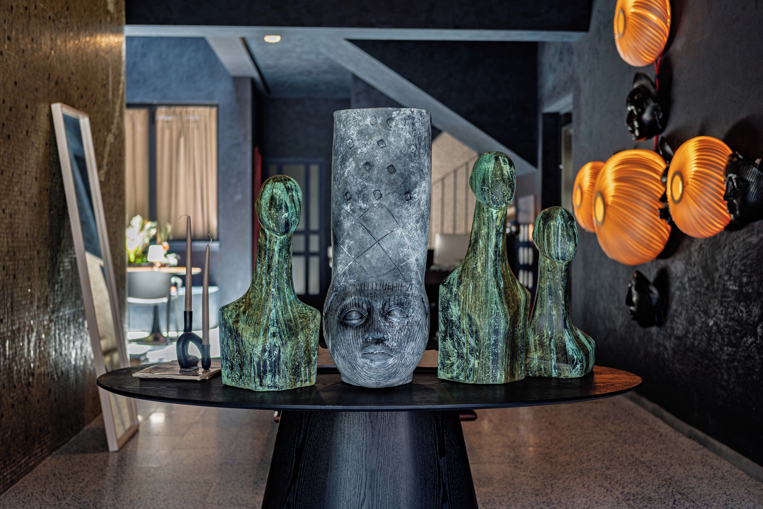 Et moderne interiør med et glasbord der viser forskellige skulpturer, og en væg med abstrakt kunst.