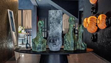 Et moderne interiør med et glasbord der viser forskellige skulpturer, og en væg med abstrakt kunst.