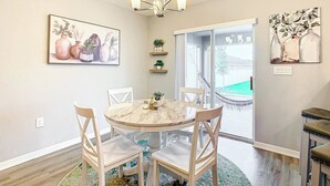 A dining area with a round table, chairs, a chandelier, and artwork on the walls. - Encanto At Auburndale (Auburndale)