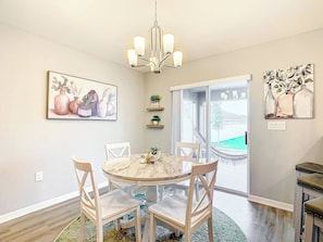 A dining area with a round table, chairs, a chandelier, and artwork on the walls. - Encanto At Auburndale (Auburndale)