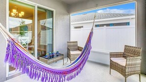 A balcony with a hammock, wicker chairs, and a view of a house. - Encanto At Auburndale (Auburndale)