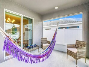 A balcony with a hammock, wicker chairs, and a view of a house. - Encanto At Auburndale (Auburndale)
