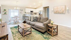 A modern living room with a sofa, coffee table, and side table, a dining area with chairs, and a kitchen in the background. - Encanto At Auburndale (Auburndale)