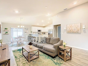 A modern living room with a sofa, coffee table, and side table, a dining area with chairs, and a kitchen in the background. - Encanto At Auburndale (Auburndale)