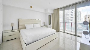 Moderni hotellihuone, jossa on suuri sänky, yöpöytä, lamppu, ikkuna, josta on näkymä rakennuksiin, sekä parveke, jossa on kaide.