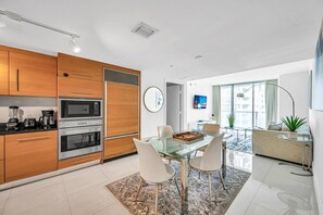 Eine moderne Küche mit integrierten Geräten, eine Essecke mit Glastisch und ein Wohnbereich mit großem Fenster.