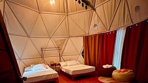 A tent-style room with two beds, a wooden floor, and a small seating area.