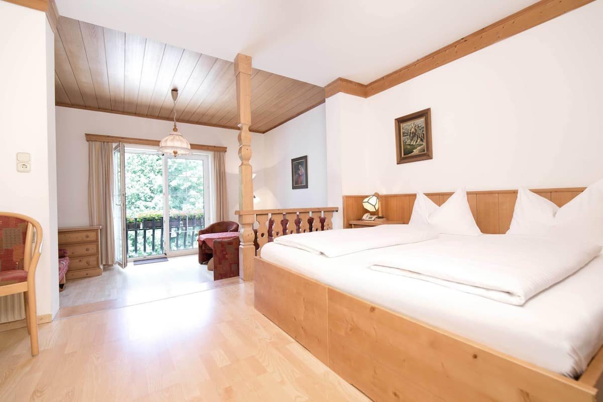 A bedroom with a large bed, wooden headboard, a wooden ceiling, a window with curtains, a chair, and a nightstand.