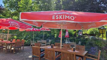 Mesas y sillas de madera al aire libre con sombrillas rojas, mostrando el nombre 'ESKIMO' en un jardín.