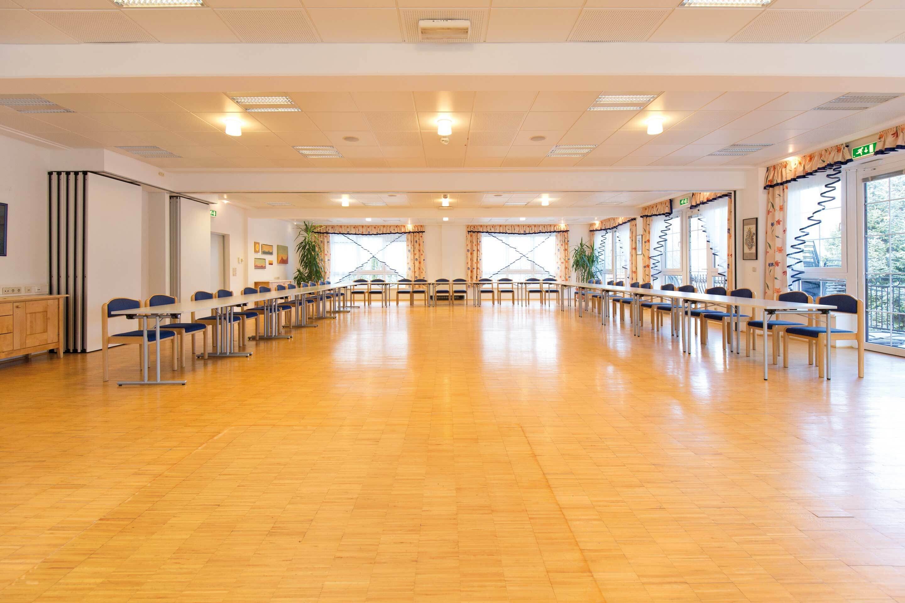 Ein Konferenzraum mit Stuhlreihen, einem langen Tisch und großen Fenstern.