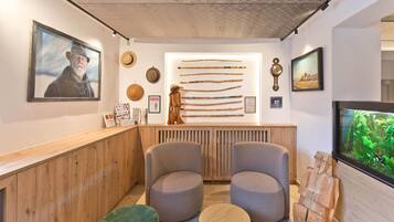 A reception area with a wooden counter, two grey armchairs, a small round table, and a television screen displaying greenery.