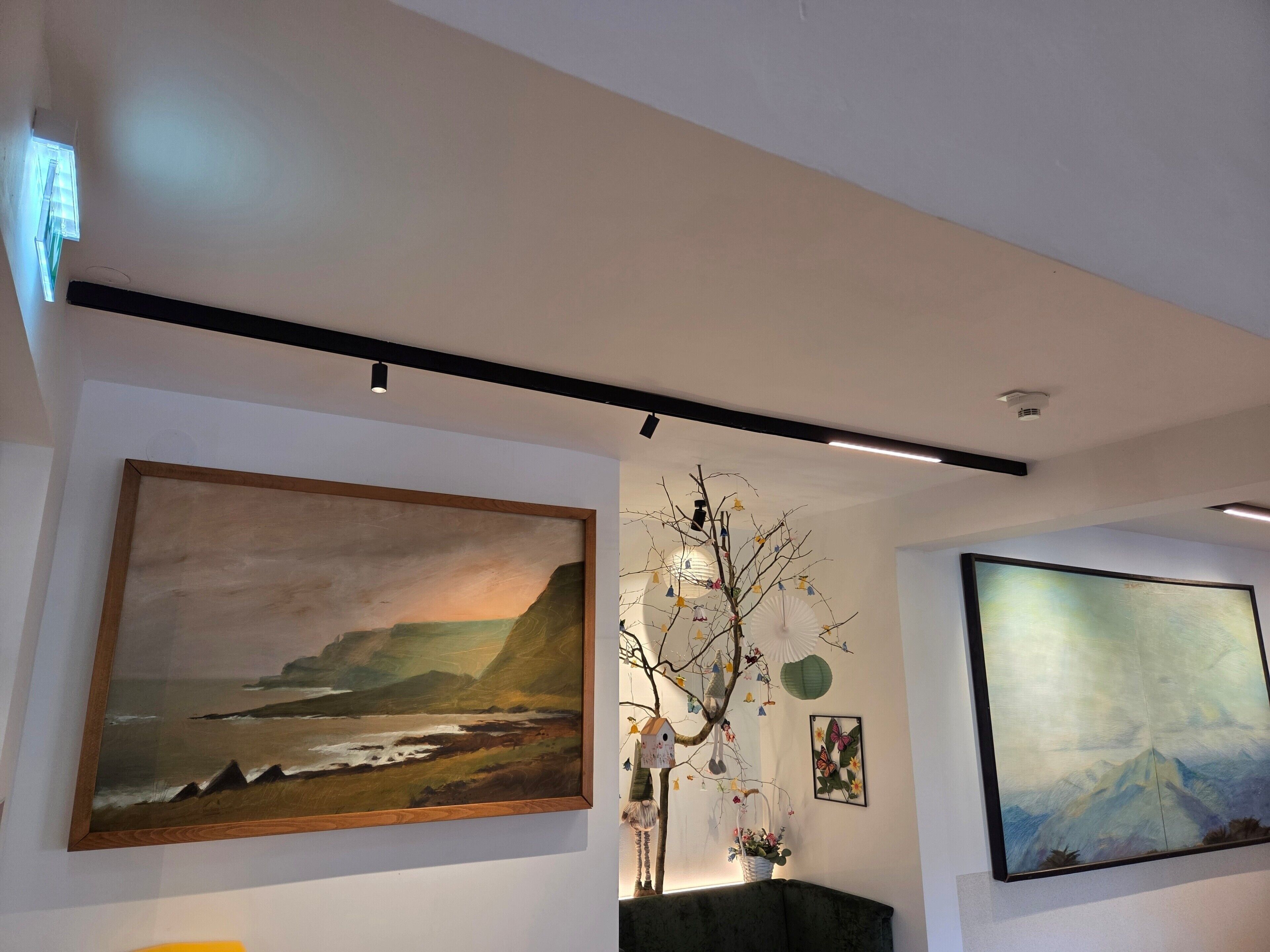 Una habitación con un cuadro grande de un paisaje, un árbol decorado con adornos, y otro cuadro en la pared.