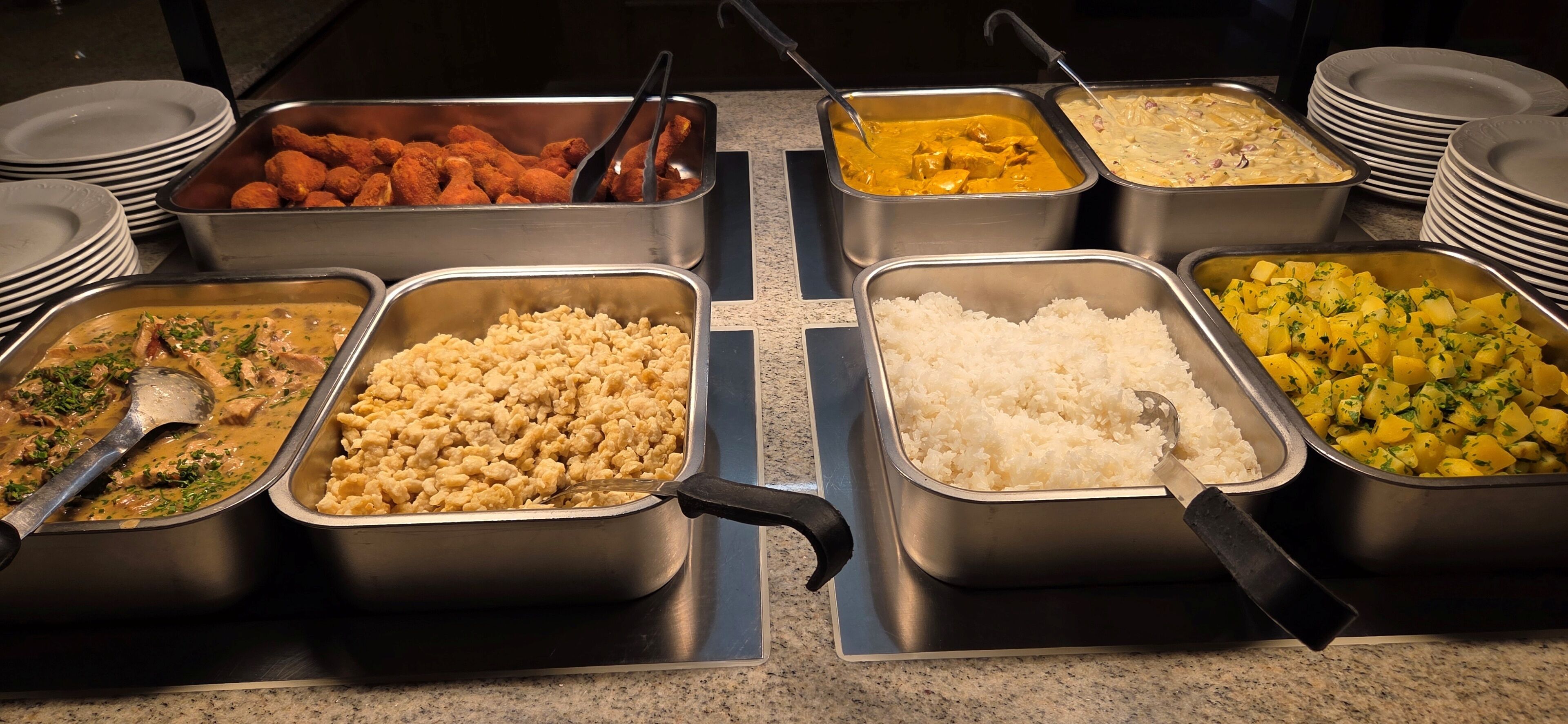 A buffet with various food options including rice, potatoes, and different dishes in metal containers.
