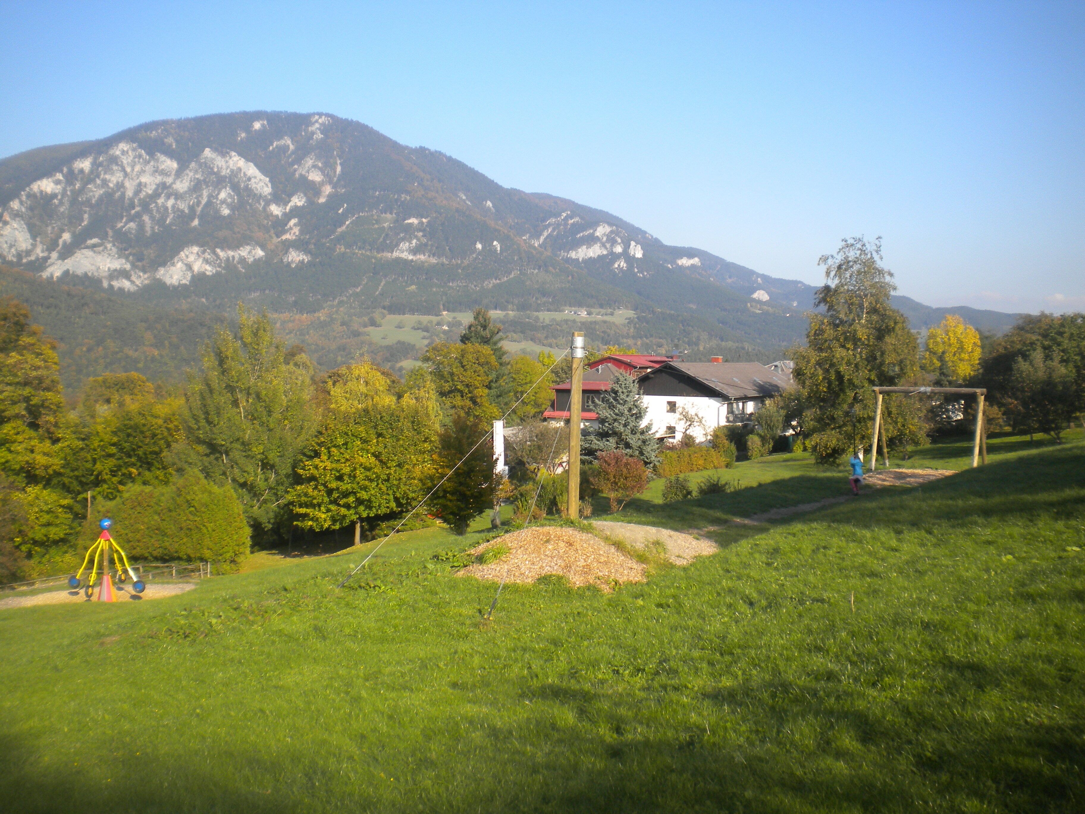 A rural landscape with a house, a swing set, and a mountain in the background.