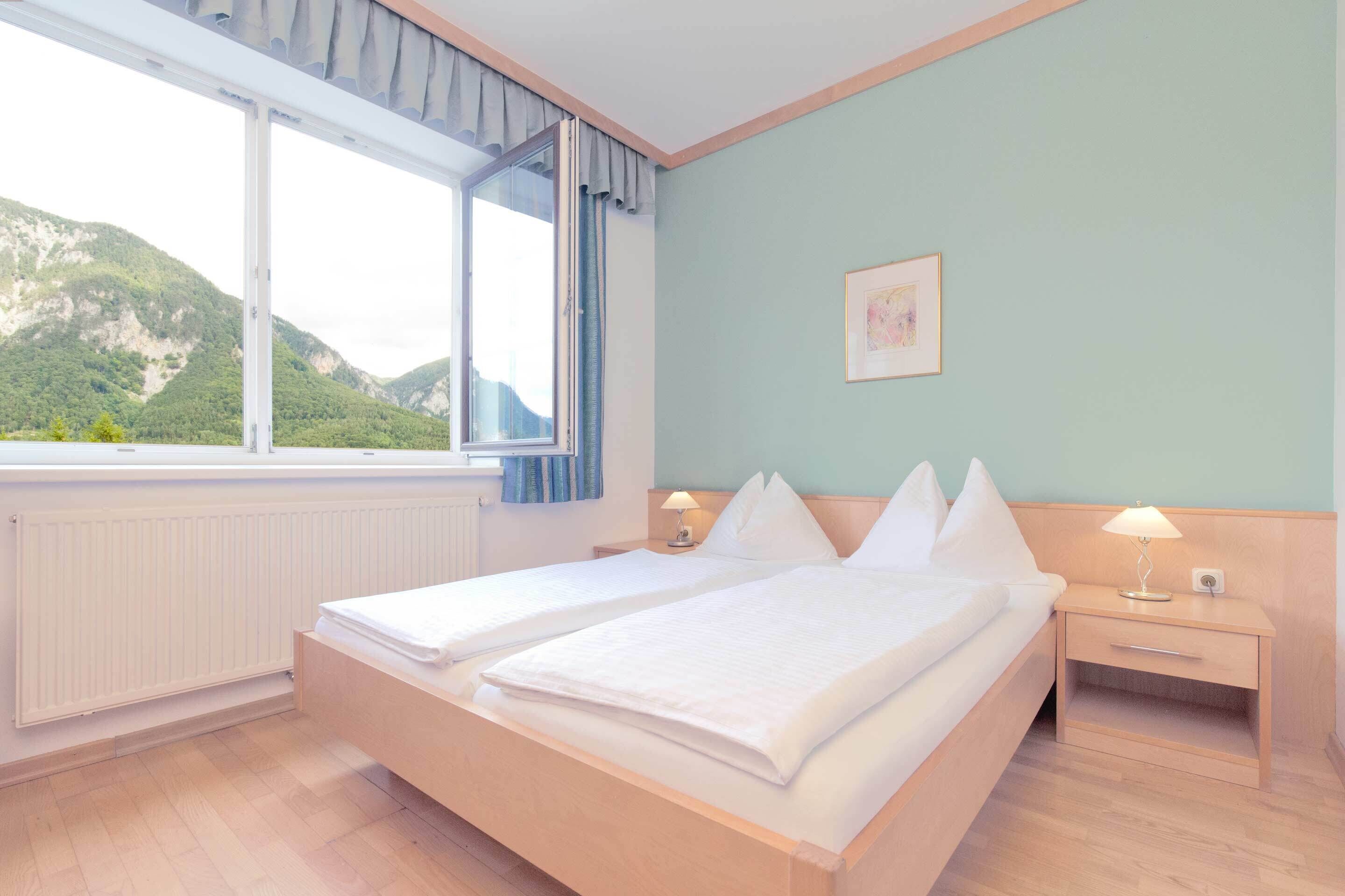 Un lit double avec du linge de lit blanc, une table de chevet avec une lampe, une fenêtre avec des rideaux et un tableau encadré au mur.