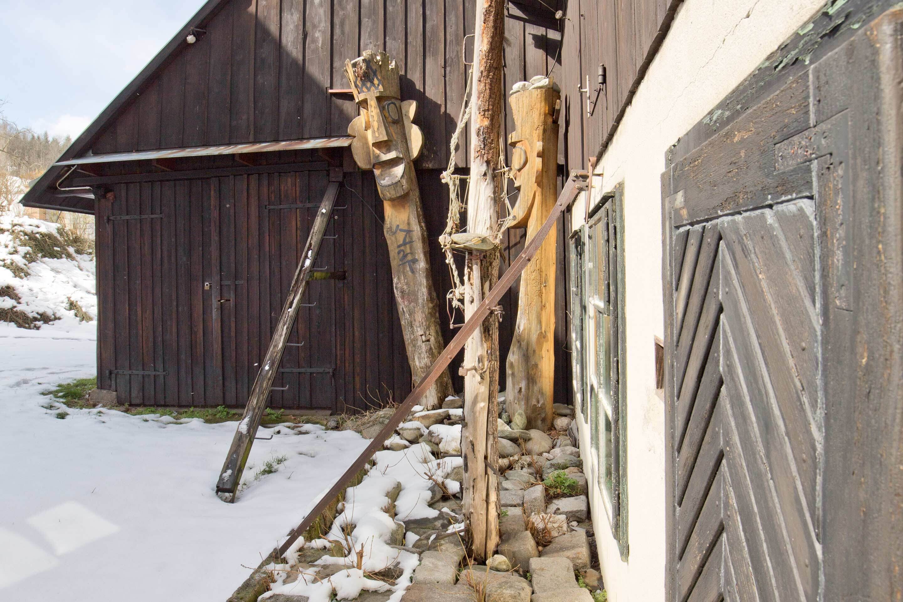 A wooden barn with a snow-covered ground, a ladder, and wooden sculptures.