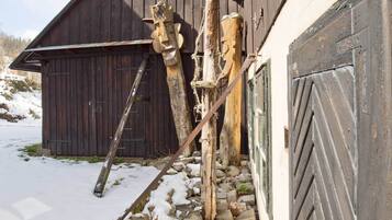 A wooden barn with a snow-covered ground, a ladder, and wooden sculptures.