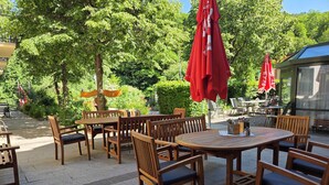 An outdoor seating area with wooden tables and chairs, red umbrellas, and greenery in the background. - Flackl - Wirt  (Reichenau an der Rax)